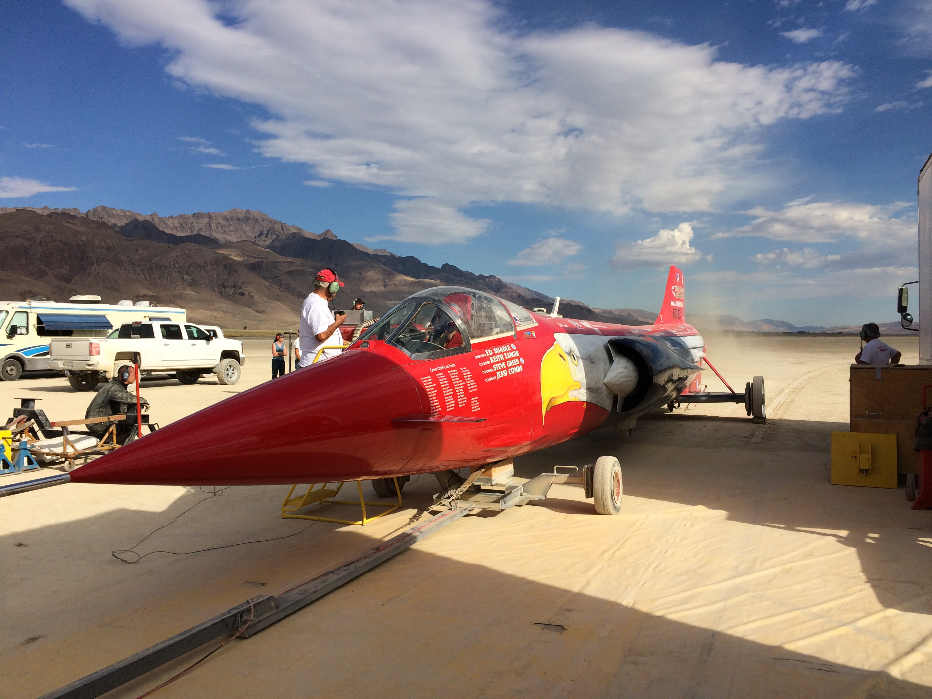 Red North American Eagle sits on desert lakebed under mostly blue sky