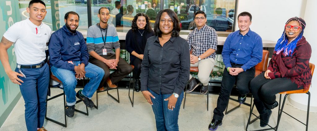 Photo of Jacky Wright standing in front of a group of smiling young people, who are seated around her in a semi-circle