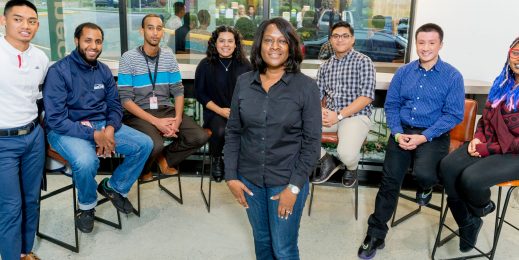 Photo of Jacky Wright standing in front of a group of smiling young people, who are seated around her in a semi-circle
