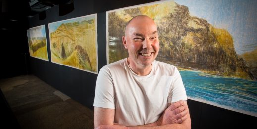 Keith Salmon smiles in front of three drawings of Hells Canyon