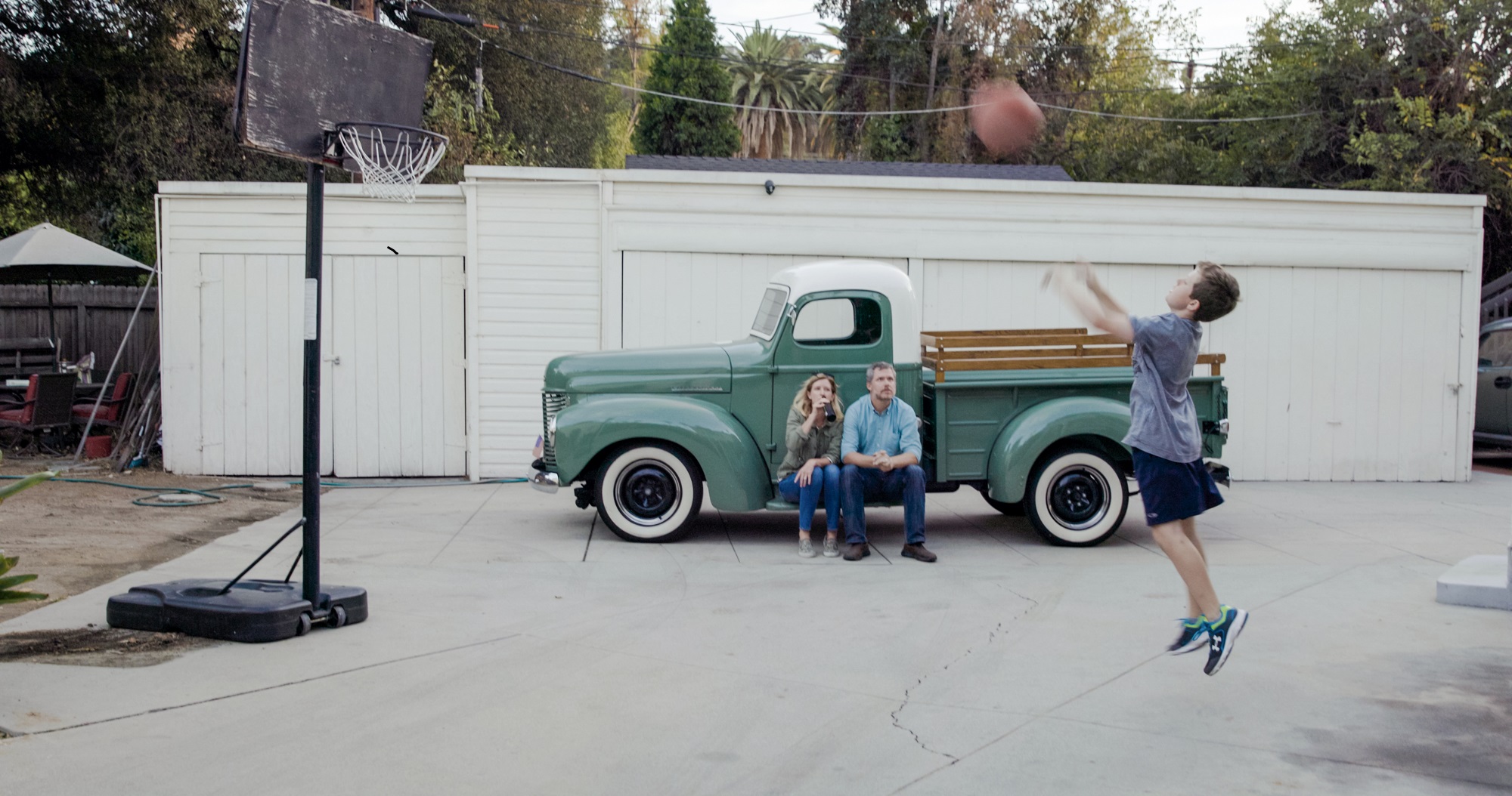 Megan and Marshall Dostal sit on running board of green vintage truck, while son Wyatt shoots a basketball