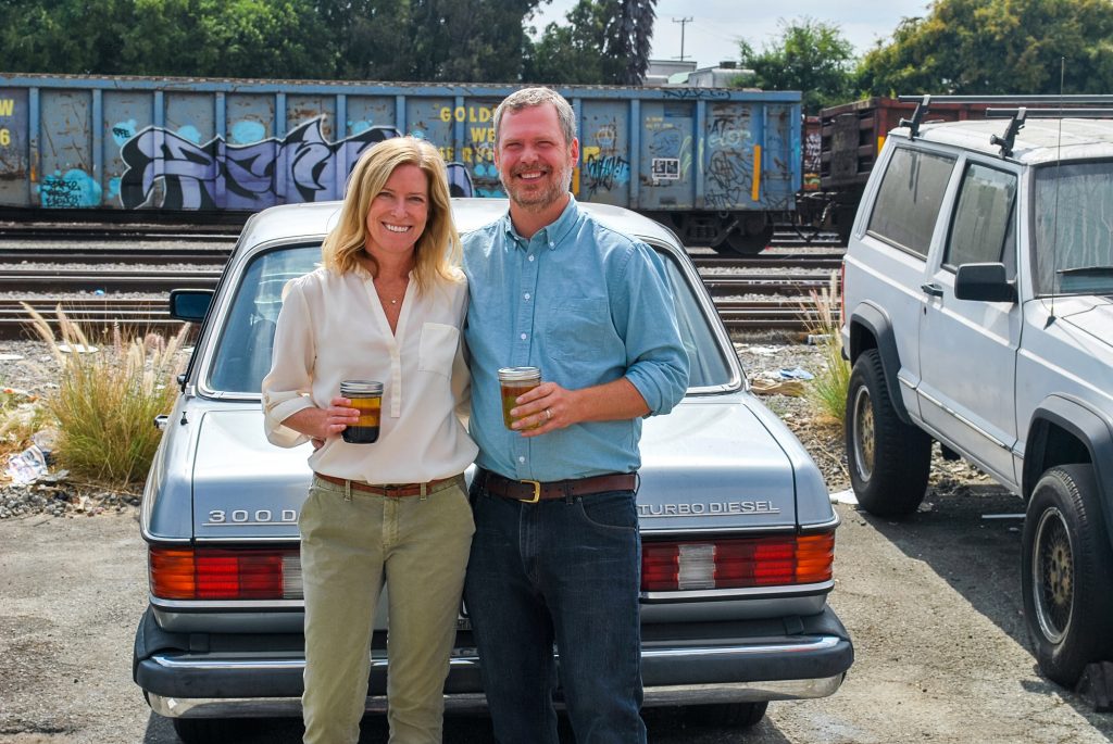 Megan and Marshall Dostal hold jars of grease in front of Marshall's Mercedes 300D