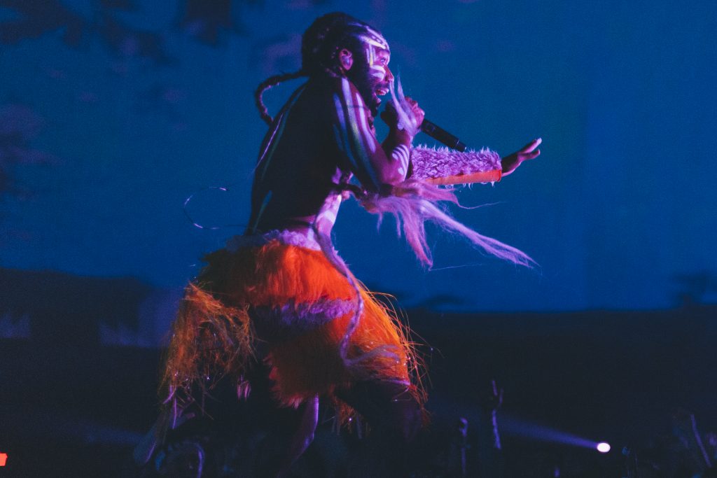 Donald Glover dressed in tribal garb, singing on stage