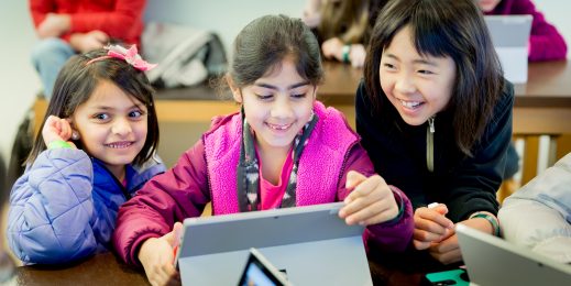 Photo of three smiling girls huddled around a Surface device