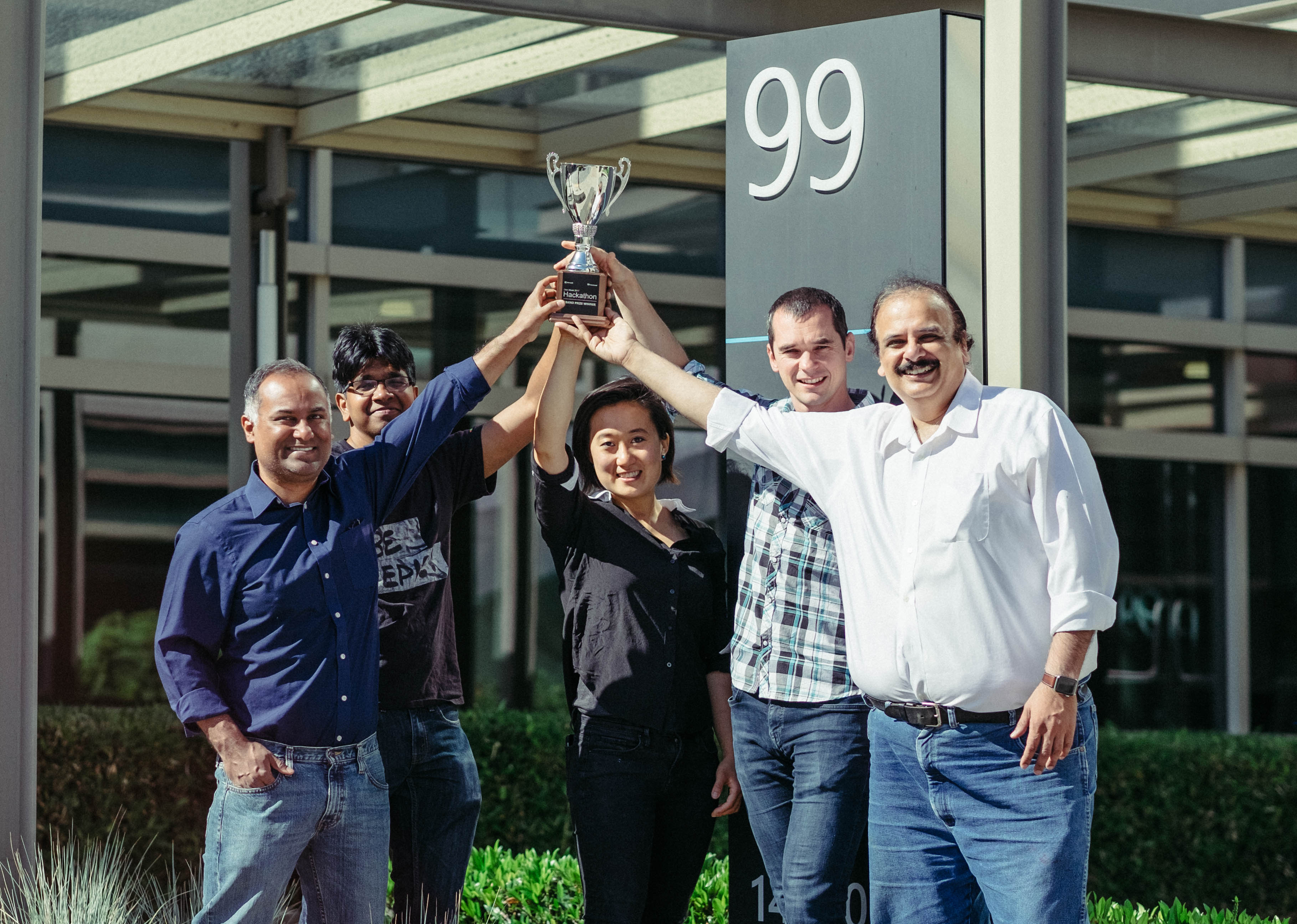 The five members of the winning Hackathon 2017 team (four men and one woman) stand in a semi-circle holding the trophy aloft.