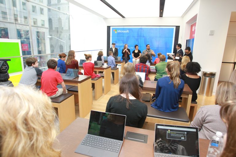 An audience of teenagers watch a presentation on stage in a Microsoft Store
