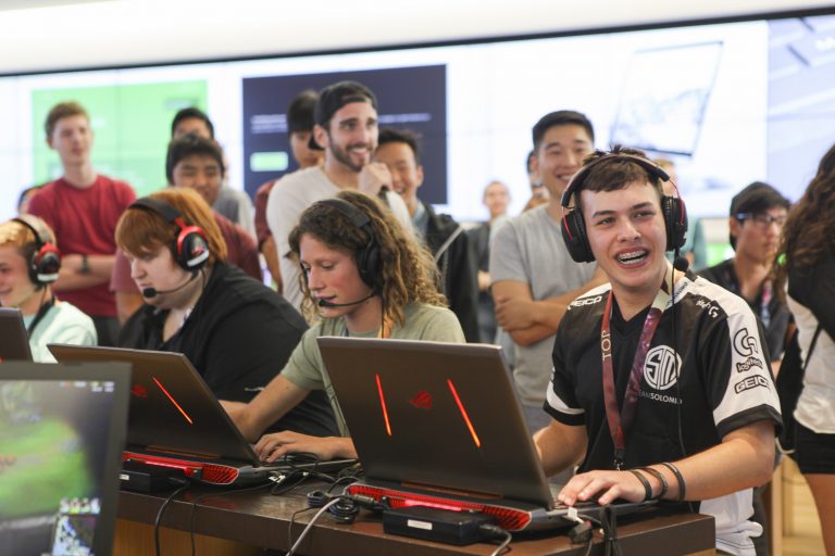 young men wearing headsets sit in front of laptops