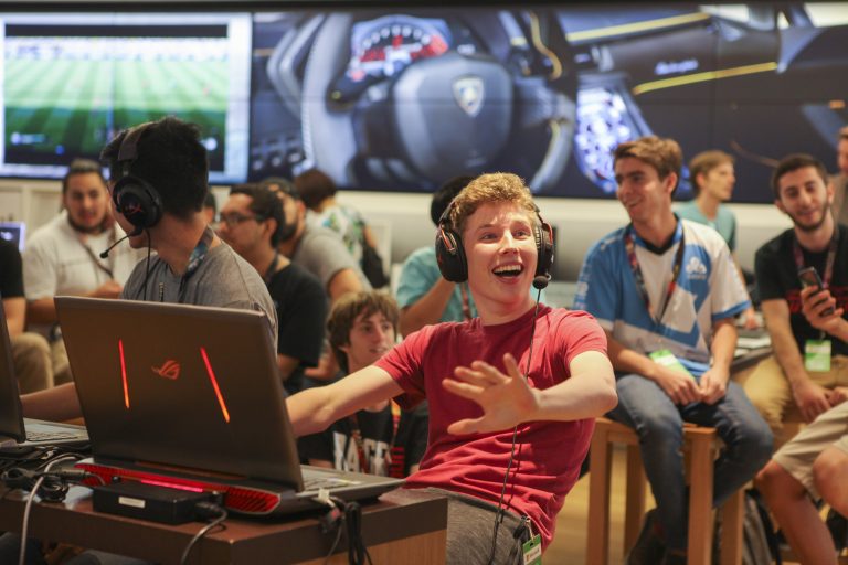 A smiling young man wears headphones and sits behind a laptop