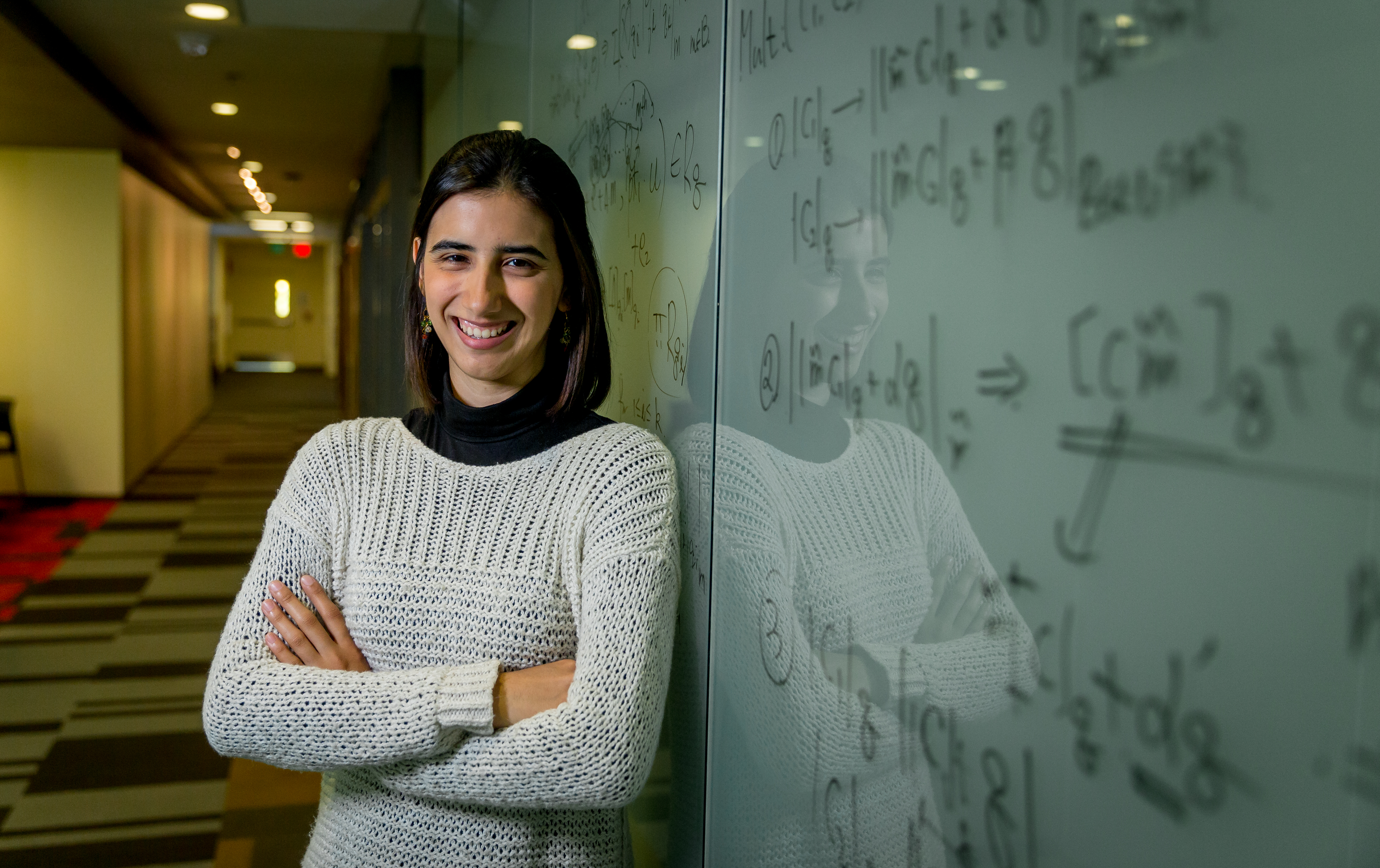 Edaena Salinas Jasso stands with arms folded against a white board filled with calculations.
