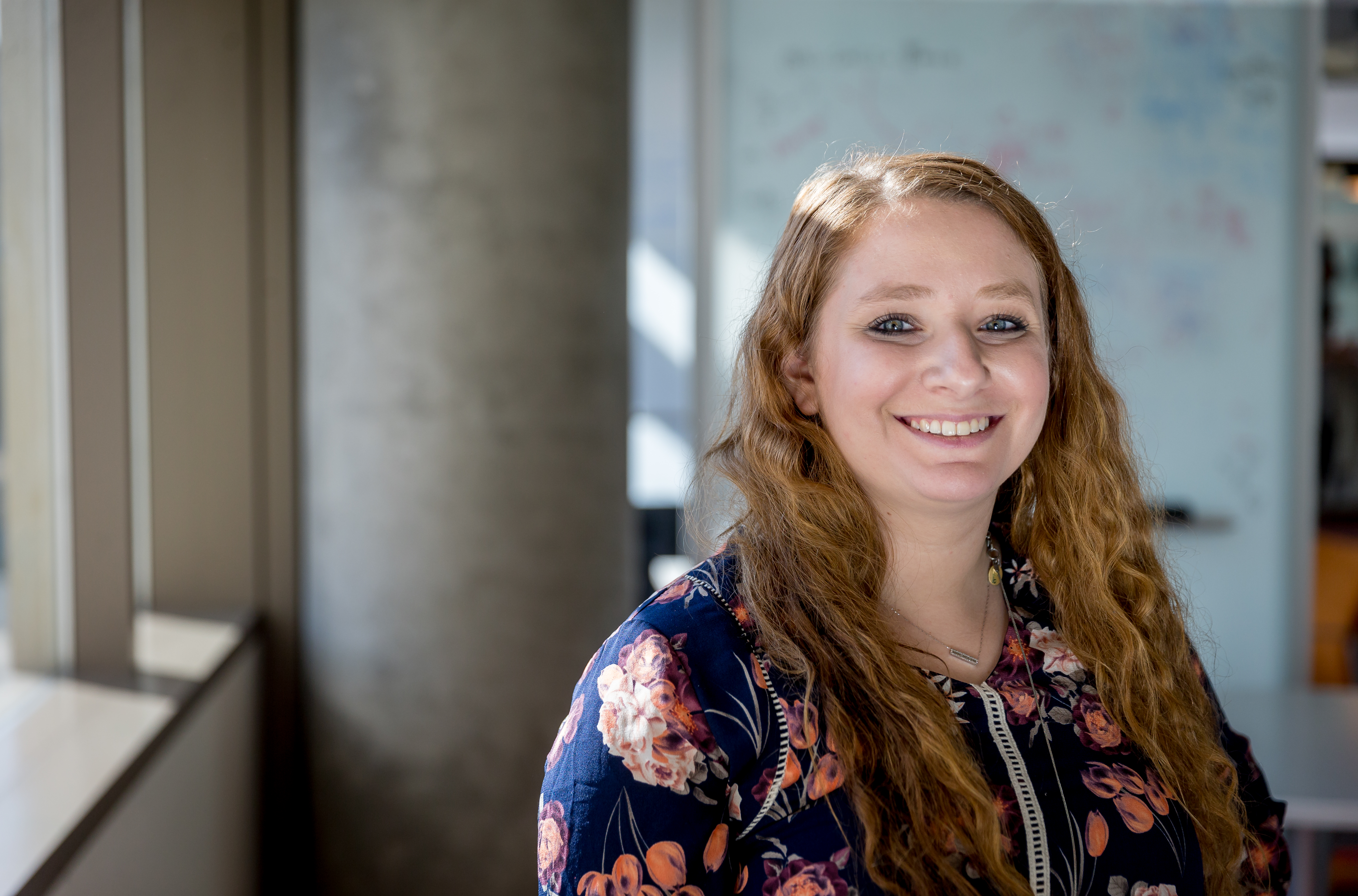 Heather Shapiro stands smiling, wearing a blue dress with a floral print