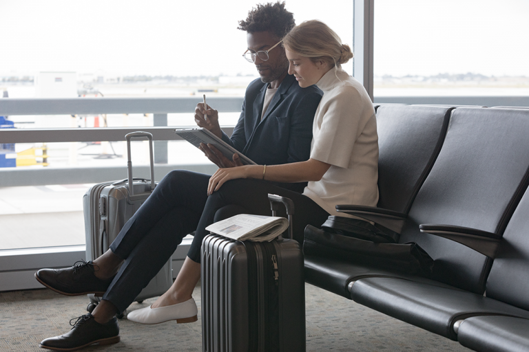 A man and a woman sit in an airport using a Surface tablet
