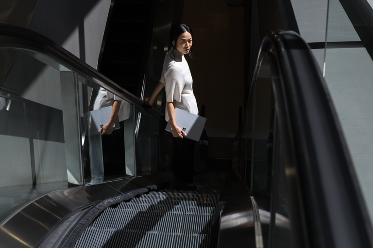 A woman holds a Surface tablet as she rides an escalator