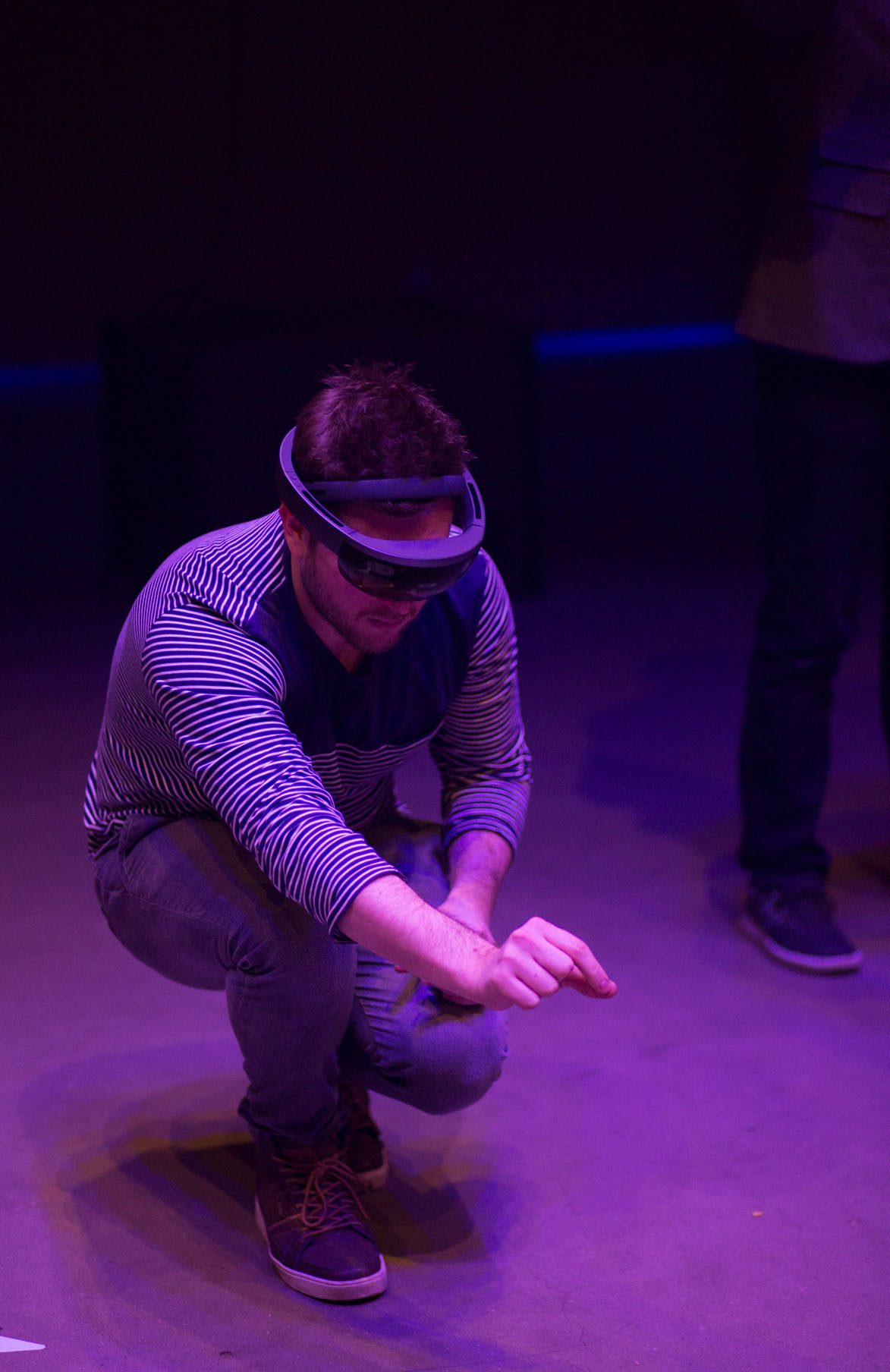 A man wearing a HoloLens device is crouching and has his arm outstretched with his hand in a pinching motion.