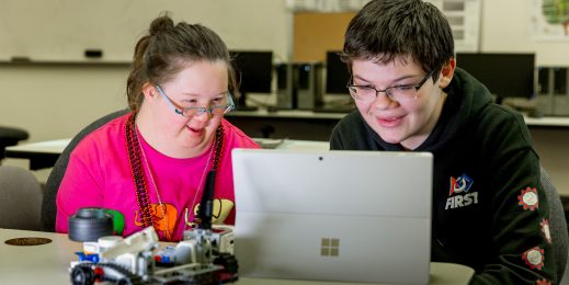 Image of a teenage girl and boy sitting looking at a computer as they design their robot.