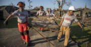 Four people carry debris away from a ruined home.