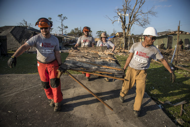Four people carry debris away from a ruined home.