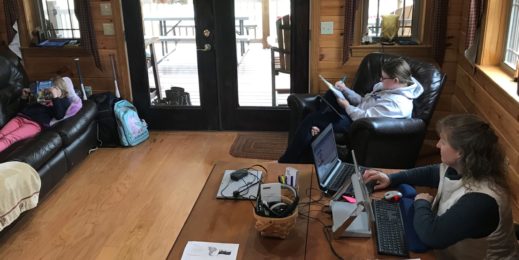 A woman works on her laptop in her home as her daughters study nearby