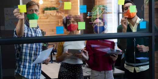 People placing sticky notes on a glass panel