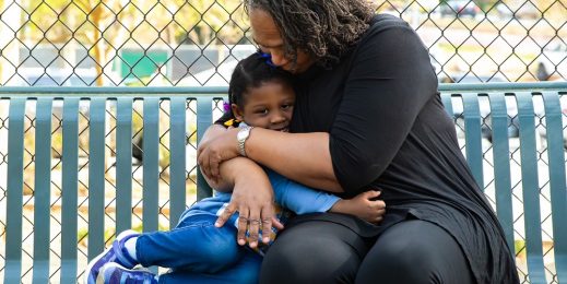 A grandmother hugs her granddaughter on a park bench