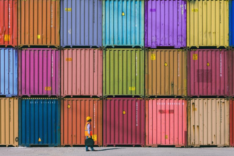 Man wearing a hardhat walking past stacks of shipping containers