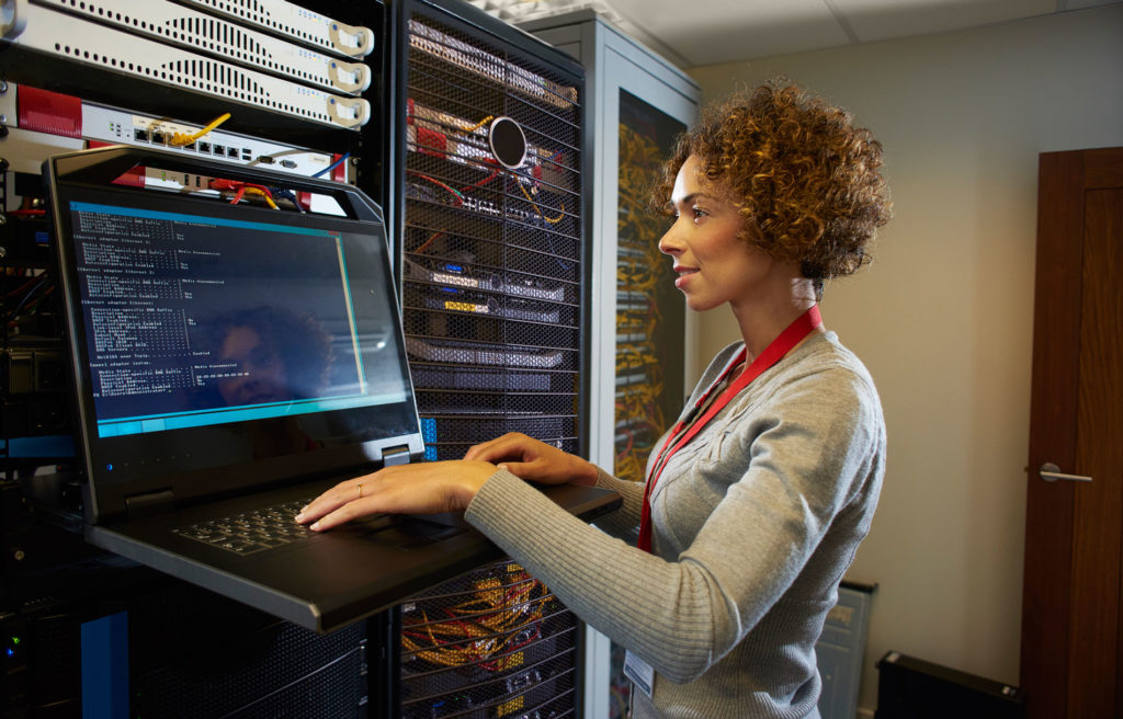 Woman standing near server with hands on laptop.