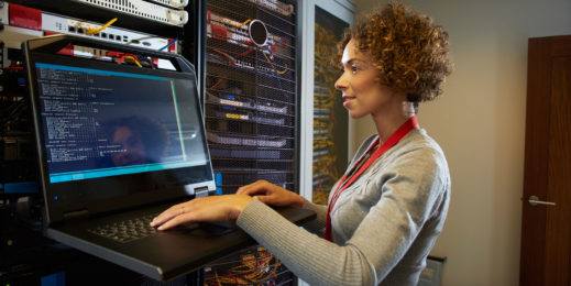 Woman standing near server with hands on laptop.