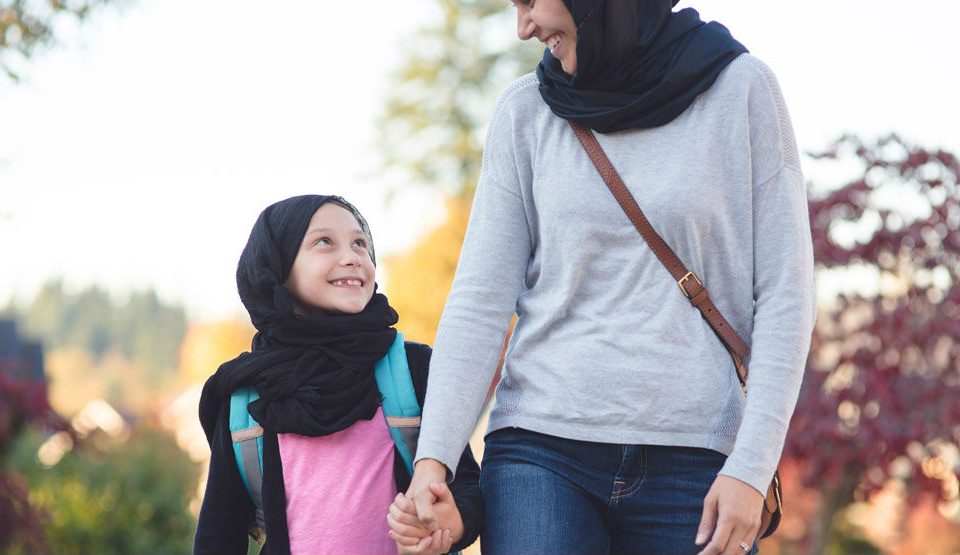 young girl holding hands looking up smiling at a woman
