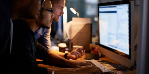 Three men at a desk looking at a computer working on a task together