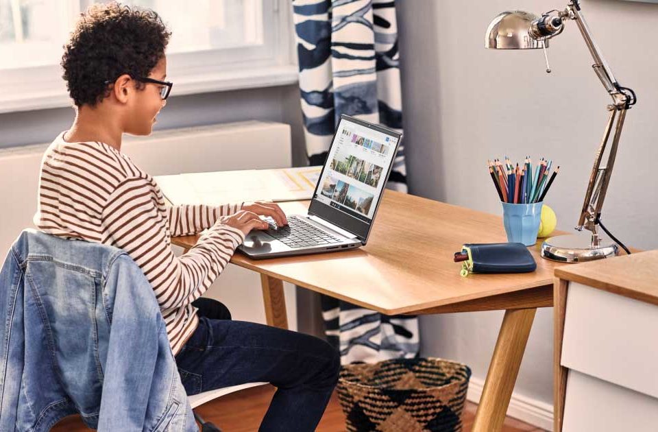 Boy sitting on a chair at his desk at home smiling while using a laptop