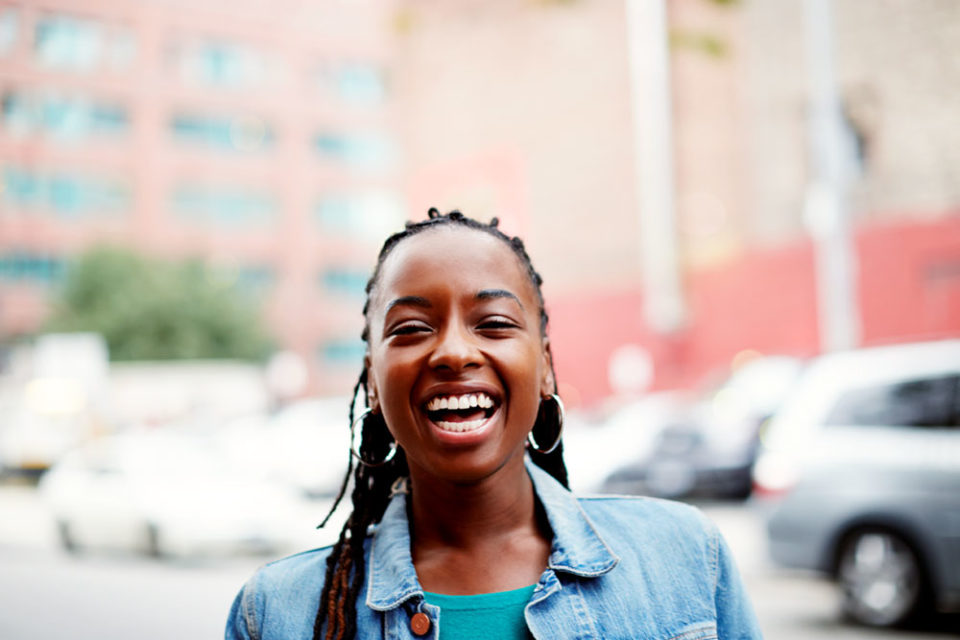 Woman in a denim jacket smiling in a city street.