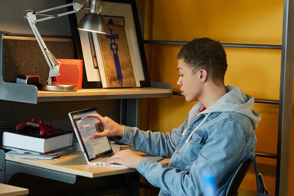 Boy sitting on chair next to desk working on laptop