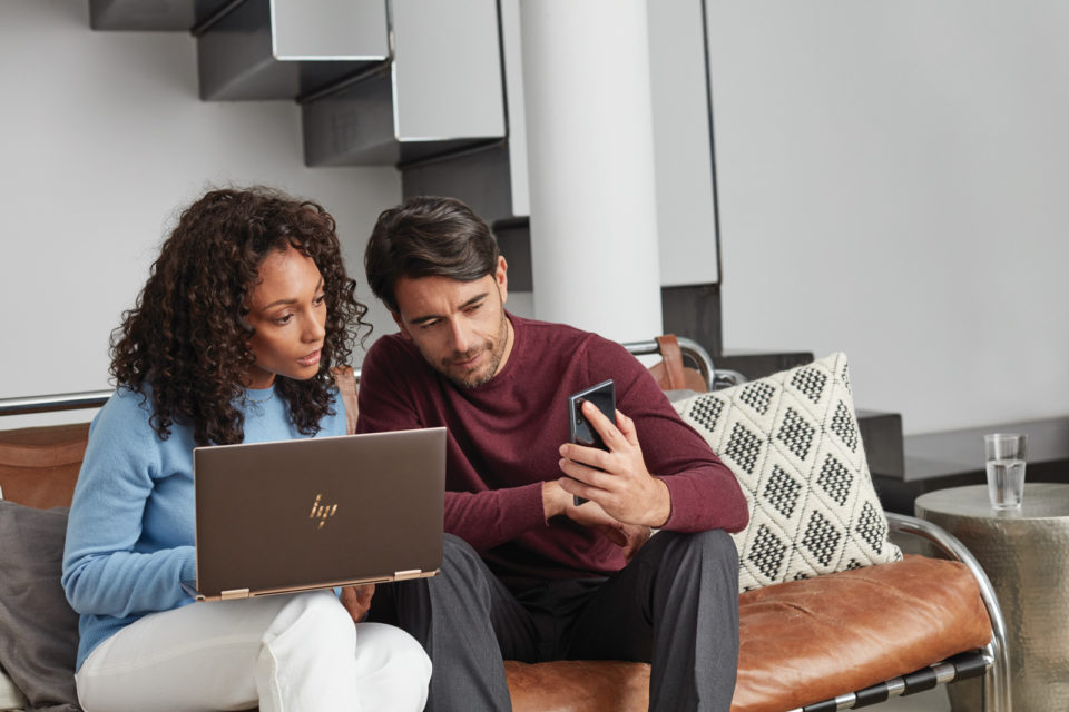 Woman in a blue shirt looking at her laptop and a man in a red shirt looking at his phone.
