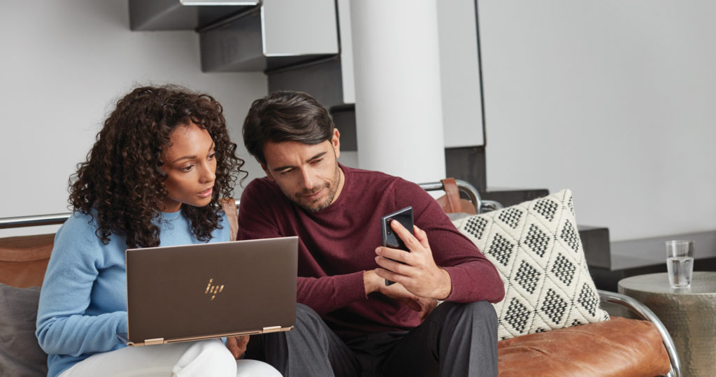 Woman in a blue shirt looking at her laptop and a man in a red shirt looking at his phone.