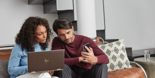 Woman in a blue shirt looking at her laptop and a man in a red shirt looking at his phone.