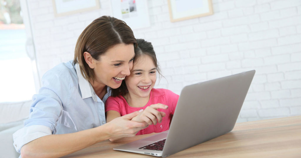 Mother assists her primary-school aged daughter during an online classroom session.