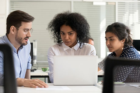 A multi-racial group of professionals collaborate on important issues – scanning a project via a laptop.