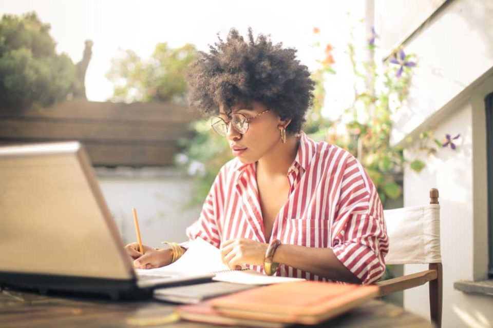 Woman in a white and red striped shirt sitting outside working at her laptop.