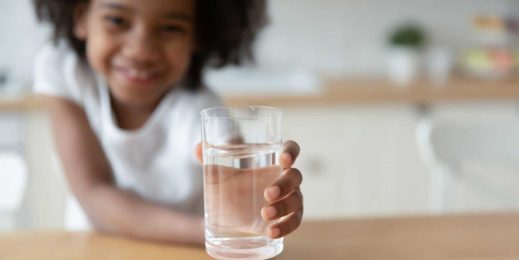 A little girl holding a refreshing glass of water in hand.