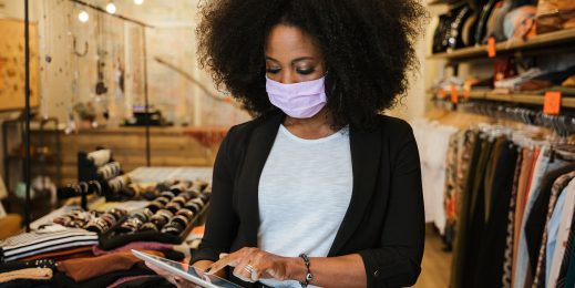 A female shop assistant wearing a face mask checks her tablet in a clothing store