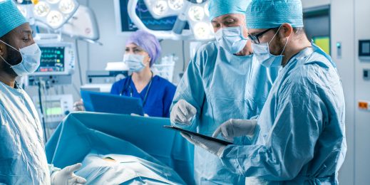 A group of medical professionals consult data from a tablet during surgery.
