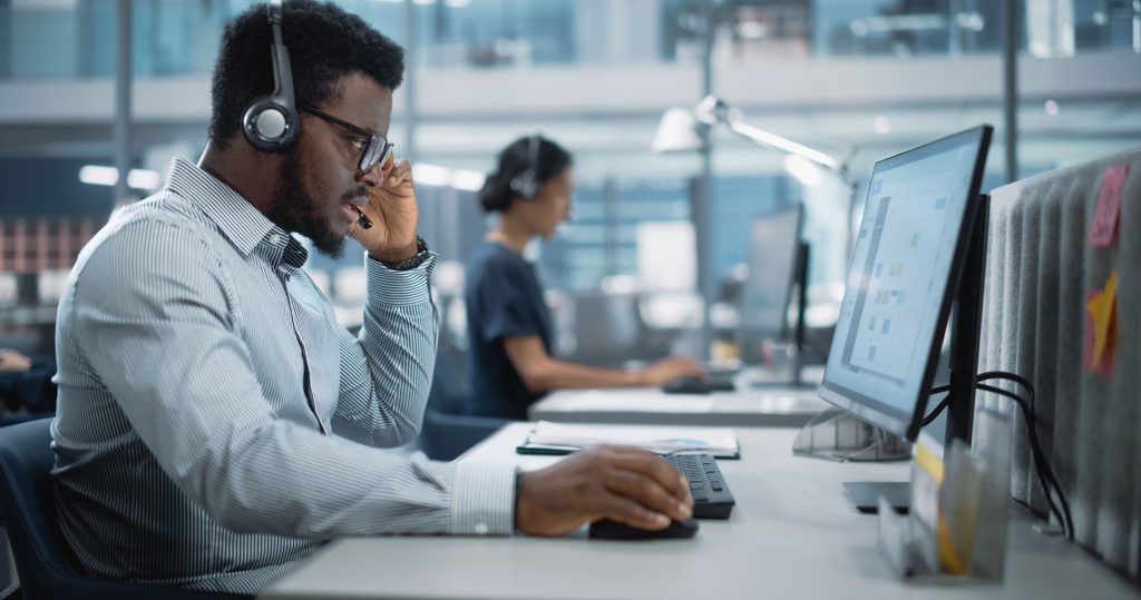 A young security professional takes a call while at work on his desktop computer