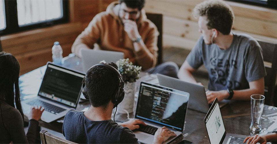 Group of four people working on laptops around a table