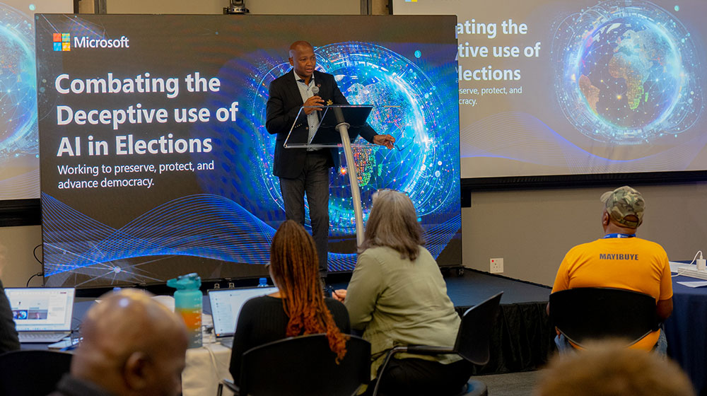 Microsoft executive in business suit addressing an audience with a screen behind him