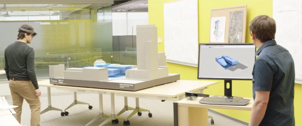 Man wears HoloLens headset and looks at architectural model, while another man looks at a computer screen