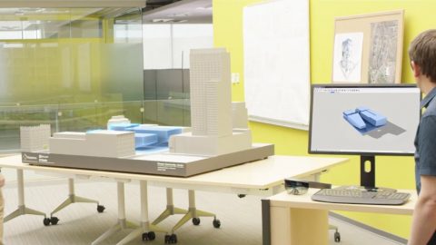 Man wears HoloLens headset and looks at architectural model, while another man looks at a computer screen