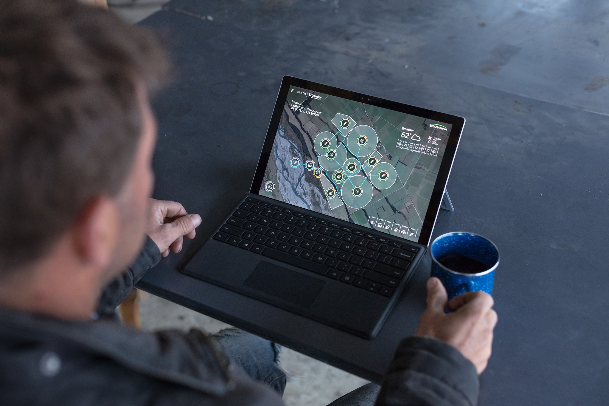 Craig Blackburn looks at overview of green farms on laptop while holding a coffee mug