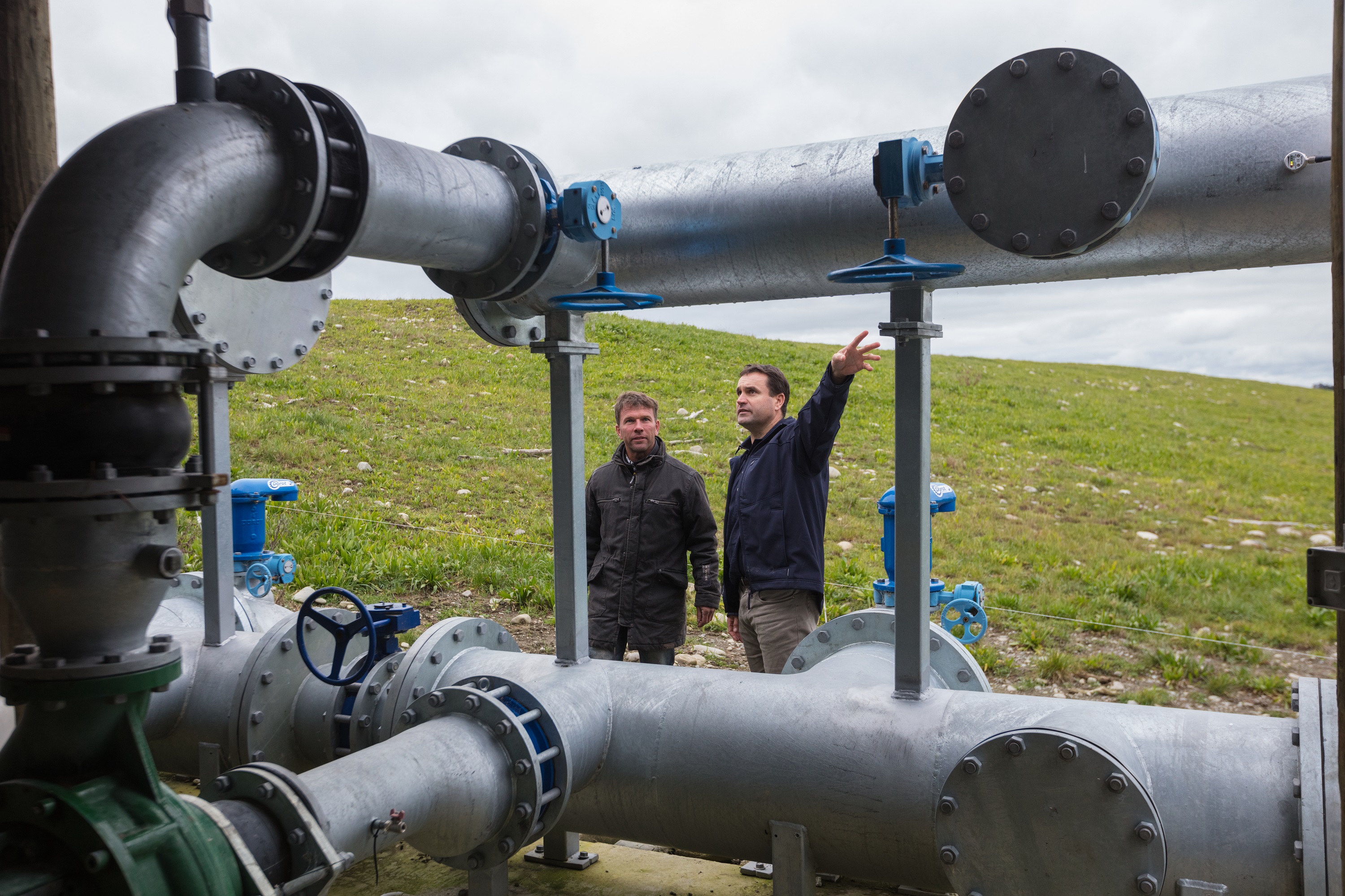 Two men look at metal water pipes in a field