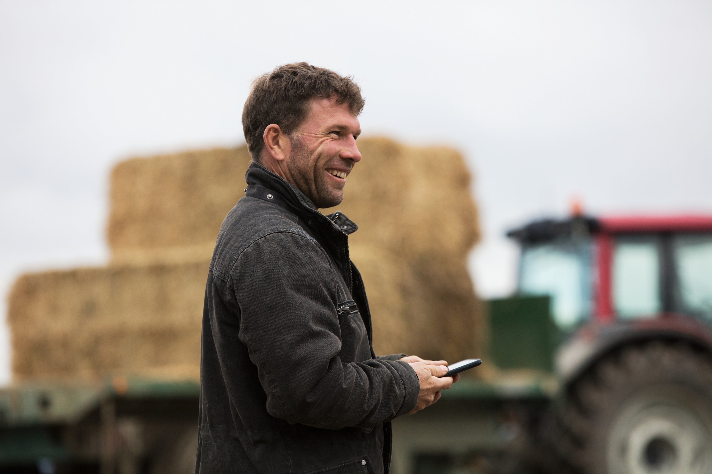 Craig Blackburn smiles while holding phone in front of farm equipment