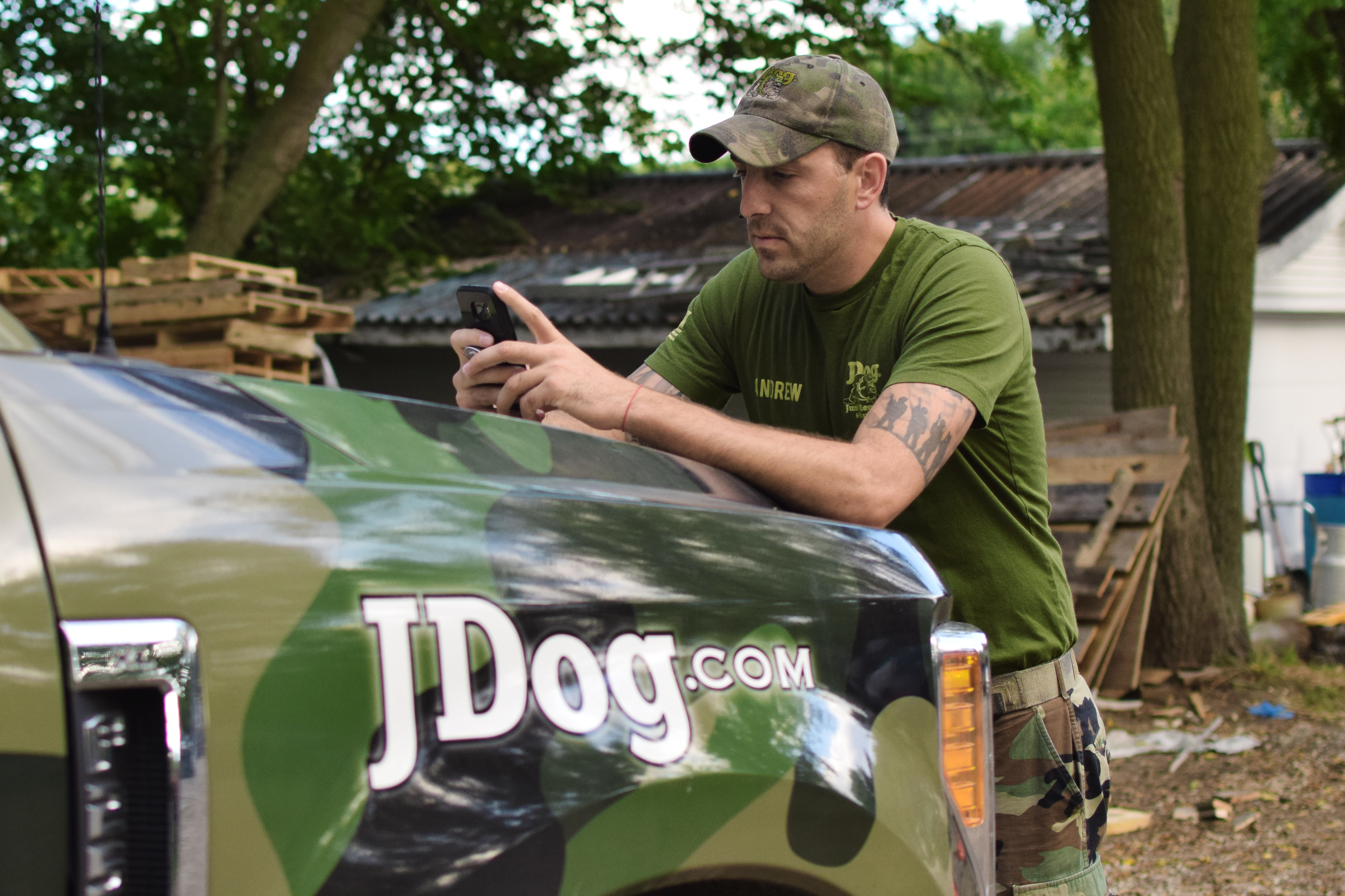 Andrew Weins conducts JDog business on his phone while leaning on the hood of his vehicle.