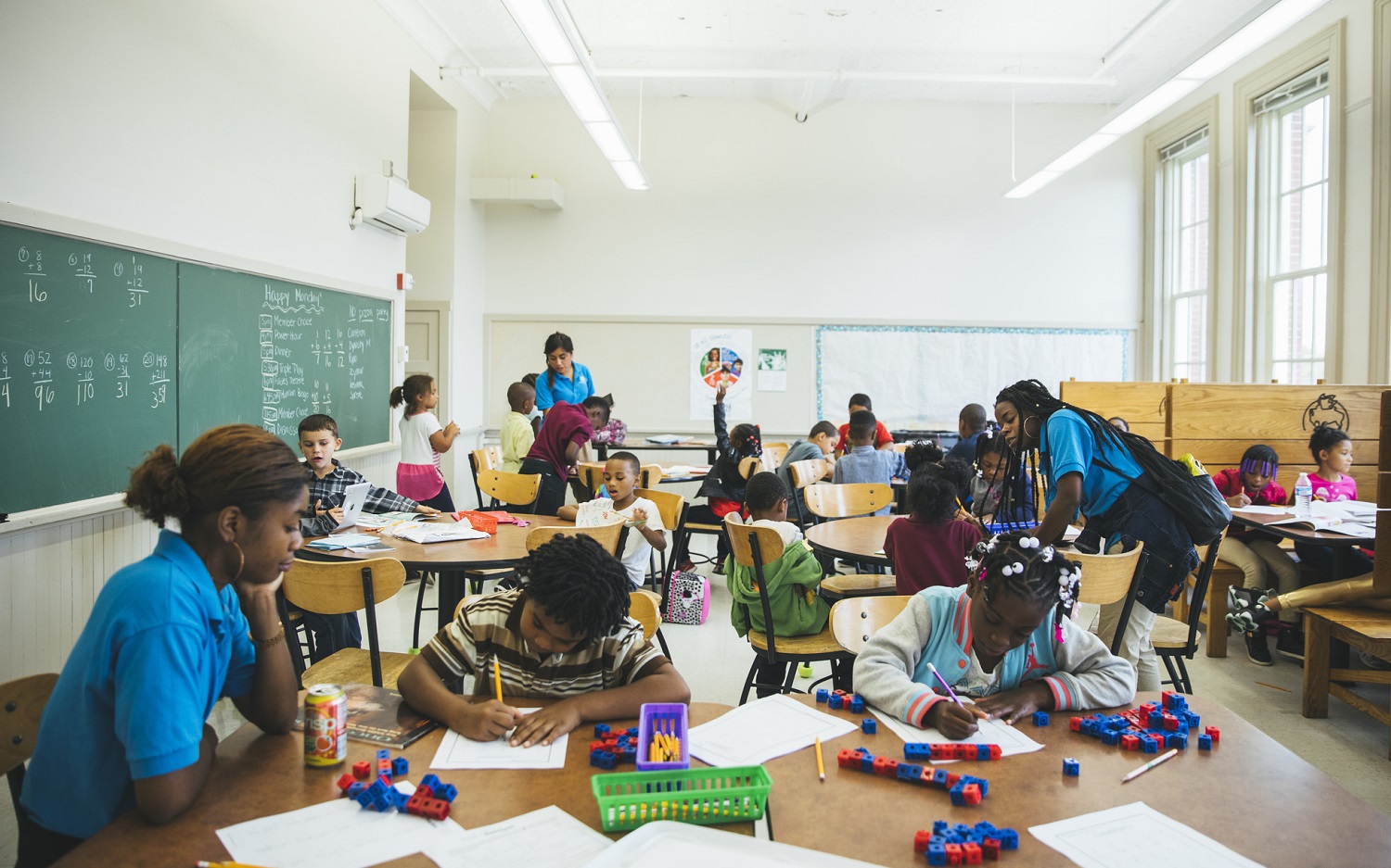 Adults help young kids with homework and learning activities with paper, blocks and pencils in large, light-filled room